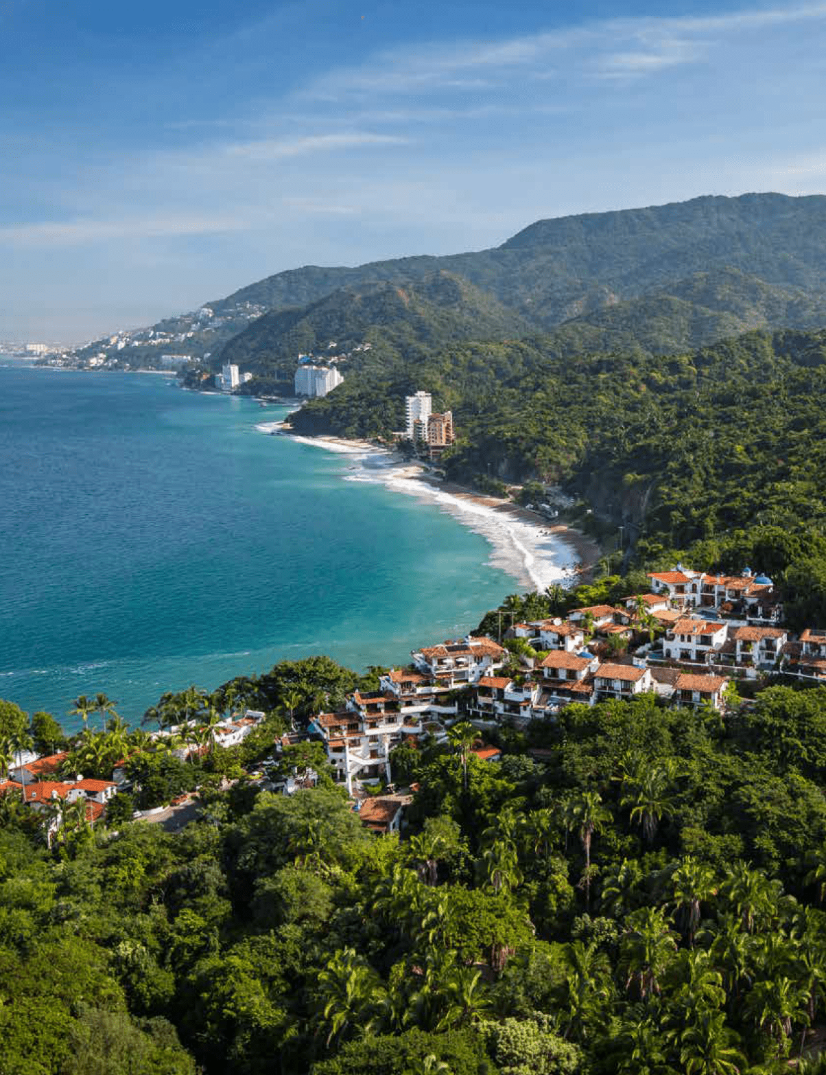 A coastal landscape with turquoise water, a sandy beach, lush green hills, and a cluster of white and terracotta-roofed buildings nestled among dense vegetation. Description generated by AI
