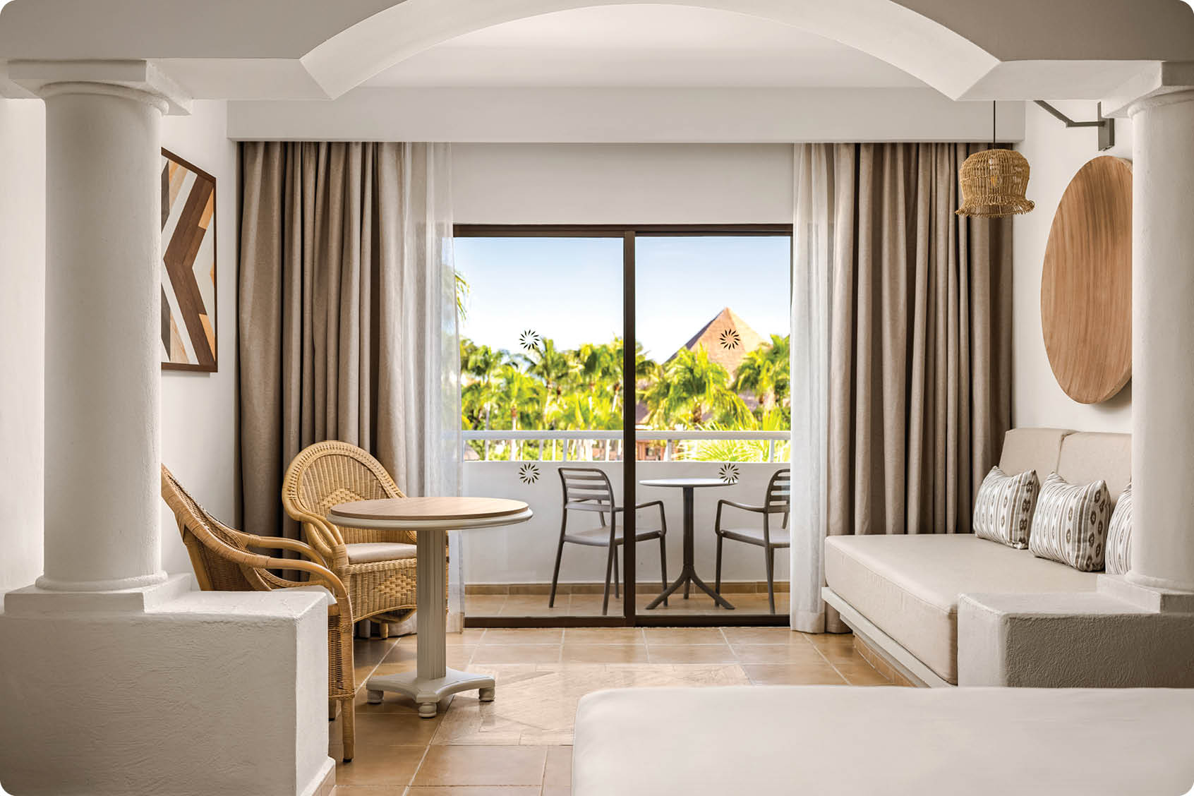 A living room with a couch, chair, and dining table. A sliding glass door is open, revealing a patio with a view of the ocean. AI generated content